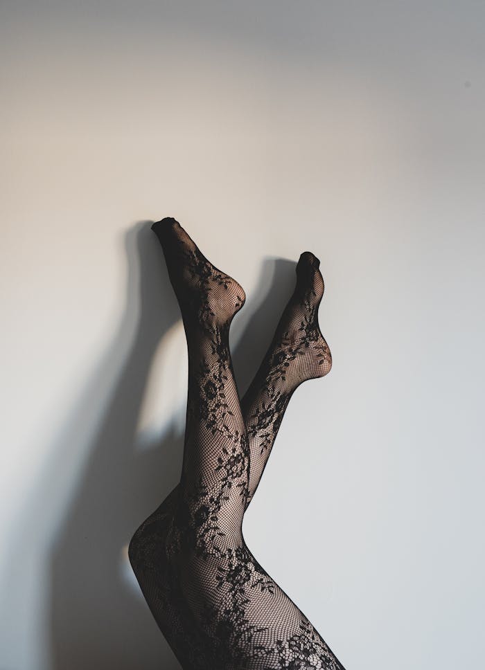 services-01 Artistic photo of female legs in lace stockings against a white wall.